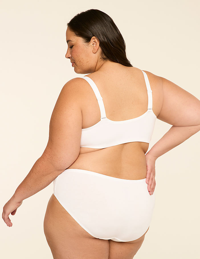 A woman in white lingerie stands with her back to the viewer against a plain, light-colored background.
