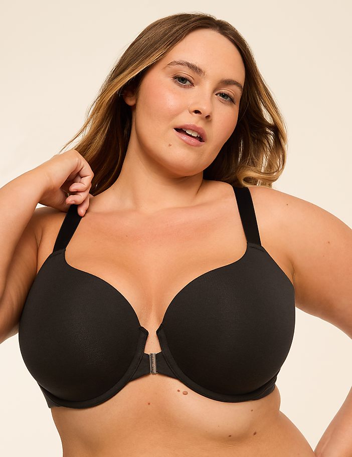 A woman with blonde hair and fair skin poses in a black bra against a plain, light-colored background.