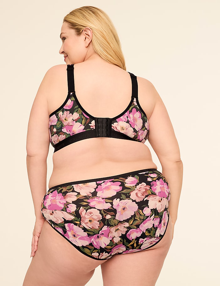 A woman in a floral bra and underwear stands against a plain, light-colored background.