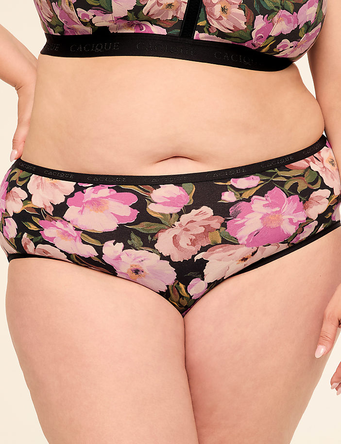 A person wearing floral print underwear and a matching bra stands against a plain background.