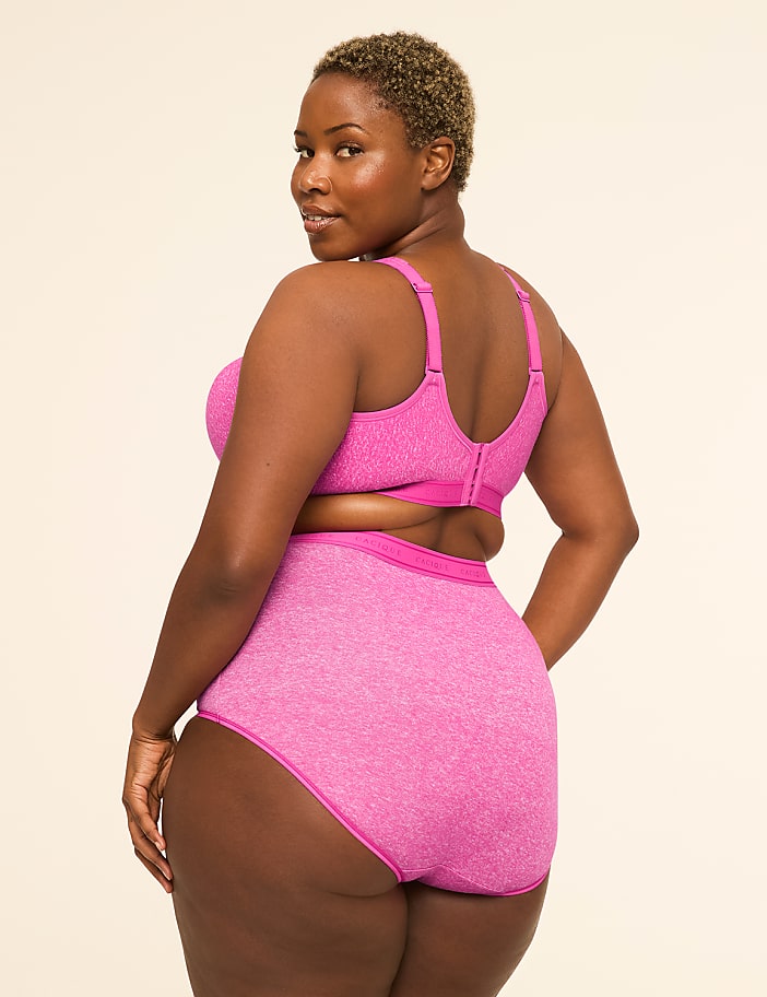 A woman in a pink bra and high-waisted underwear stands against a plain, light-colored background.