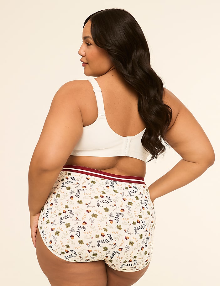 A woman in a white bra and patterned underwear stands against a plain, light-colored background.