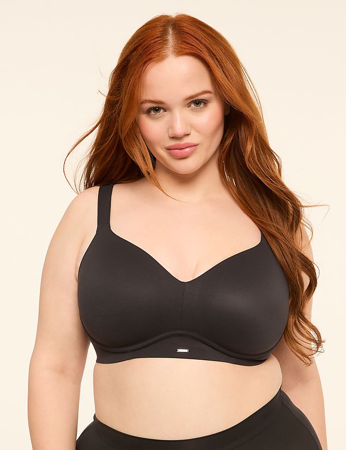 A woman with red hair and fair skin, wearing a black bra, poses against a plain, light-colored background.