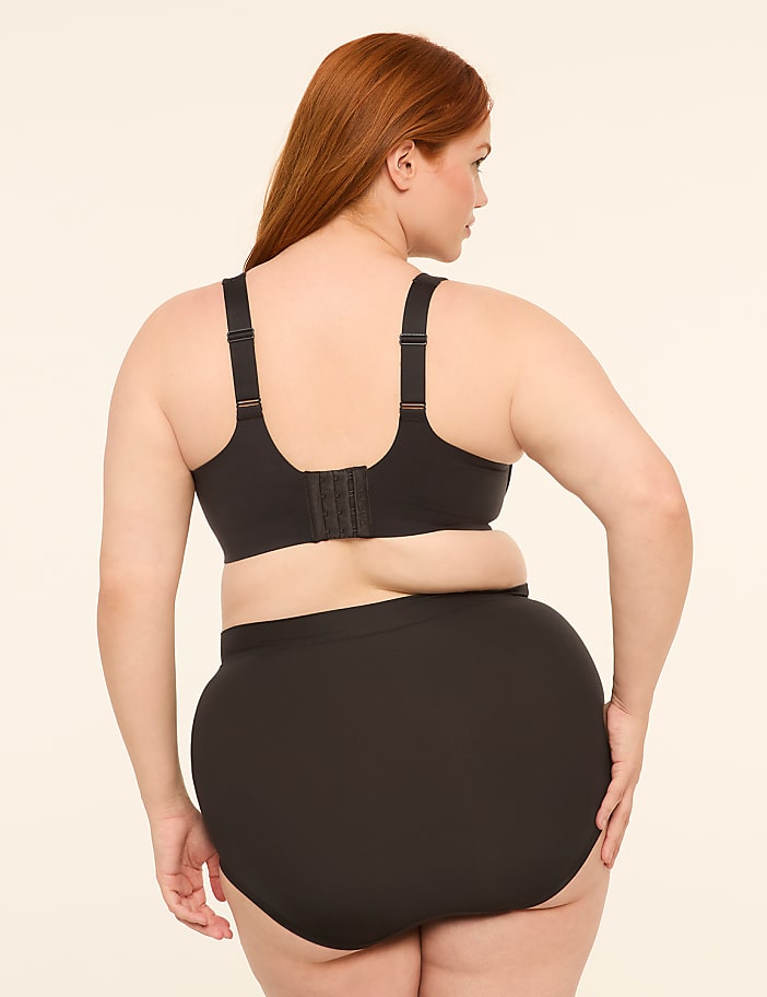 A woman with red hair is shown from the back, wearing a black bra and high-waisted briefs against a plain, light-colored background.