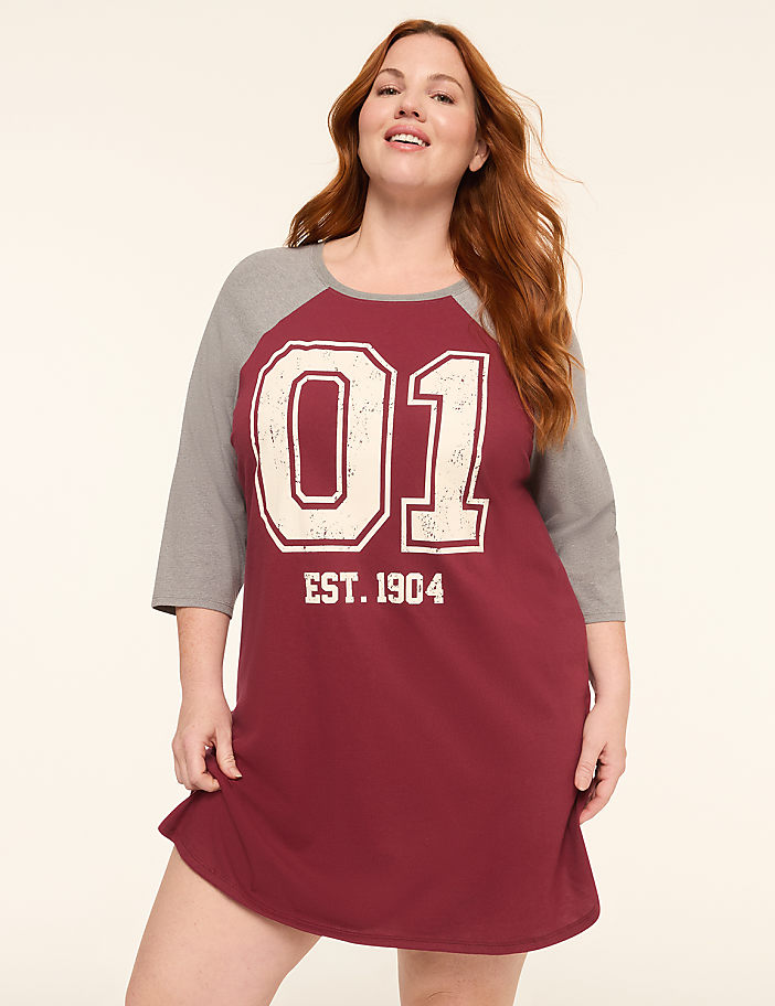 A woman with red hair smiles in a maroon and gray baseball-style nightgown with "01 EST. 1904" printed on it, against a plain, light-colored background.