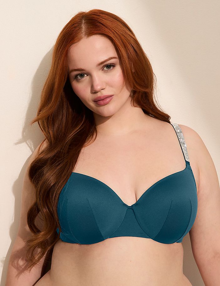 A woman with long, wavy red hair poses in a teal bikini top with embellished straps against a plain, light-colored background.