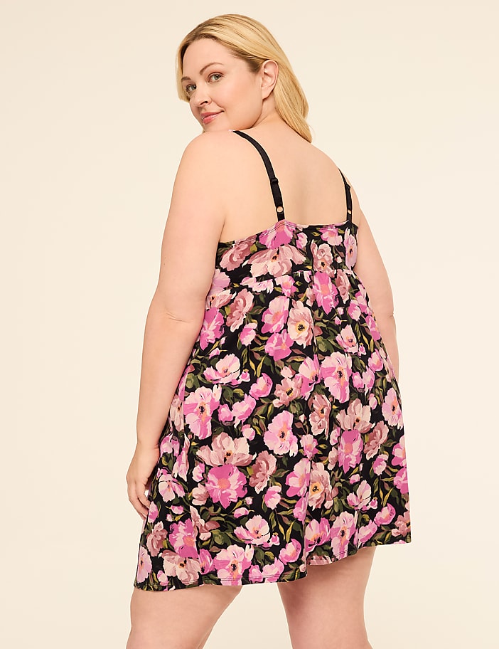 A woman in a floral dress stands against a plain, light-colored background.