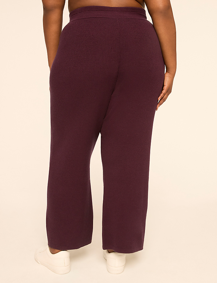 A person wearing plum-colored ribbed pants and white sneakers stands against a plain, light-colored background.