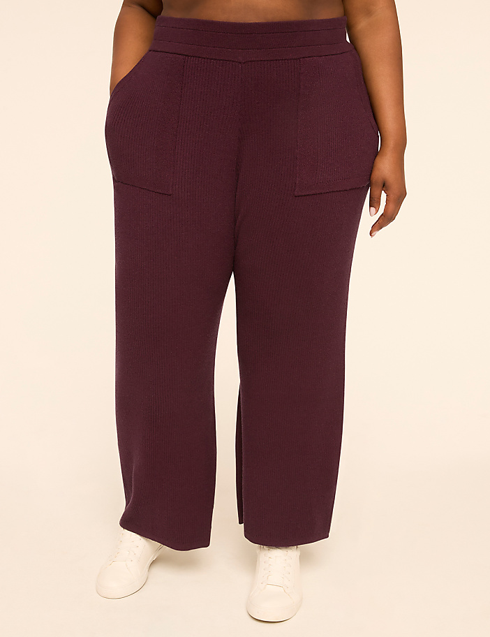 A person wearing plum-colored ribbed pants with white sneakers stands against a plain, light-colored background.