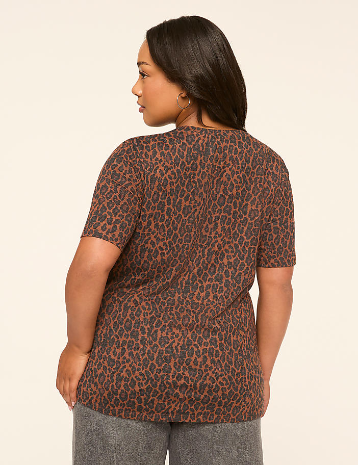 A woman in a brown leopard-print t-shirt stands against a plain, light-colored background.