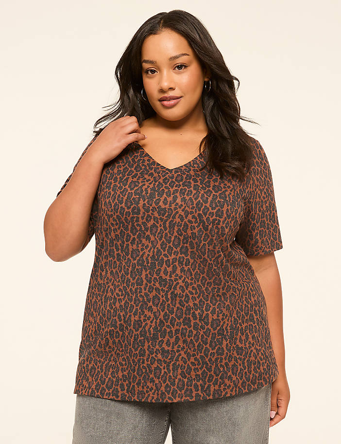 A woman in a leopard print v-neck shirt stands against a plain, light-colored background.