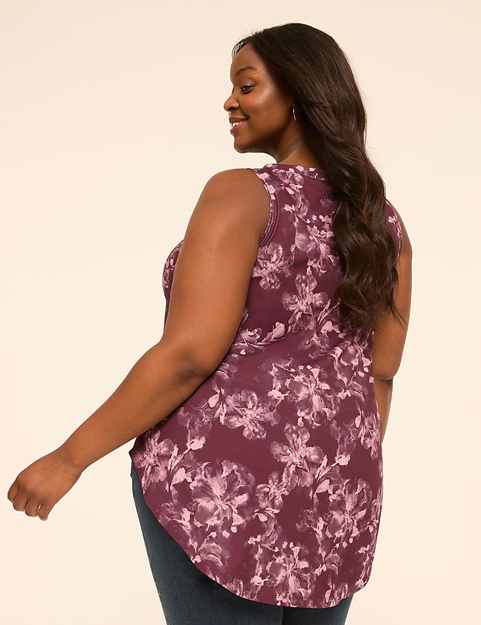 A woman in a floral top and jeans stands against a plain, light-colored background.