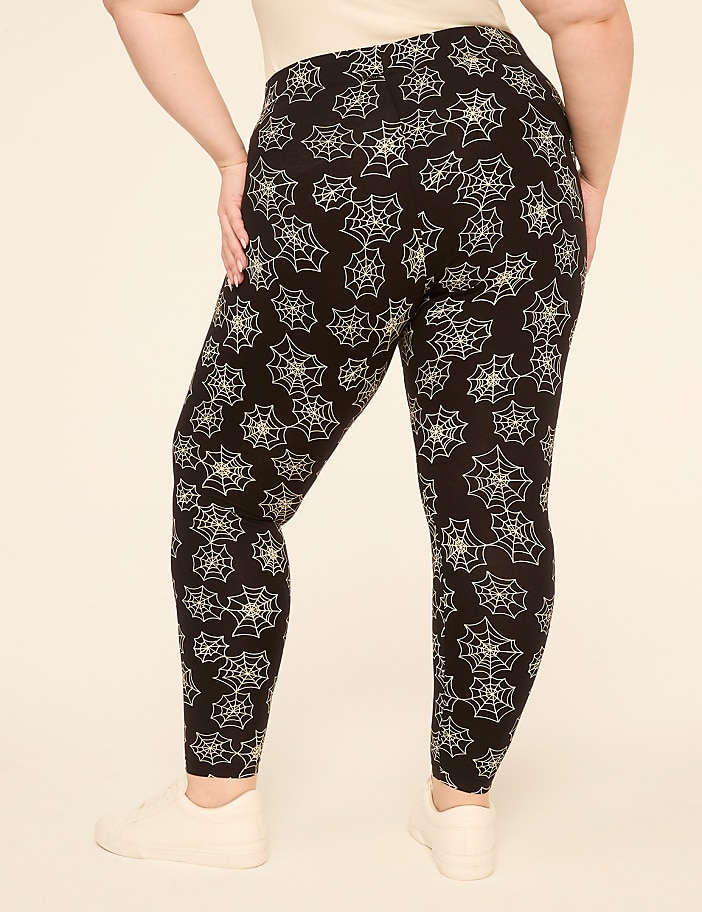 A person wearing black leggings with a white spiderweb pattern stands against a plain, light-colored background.