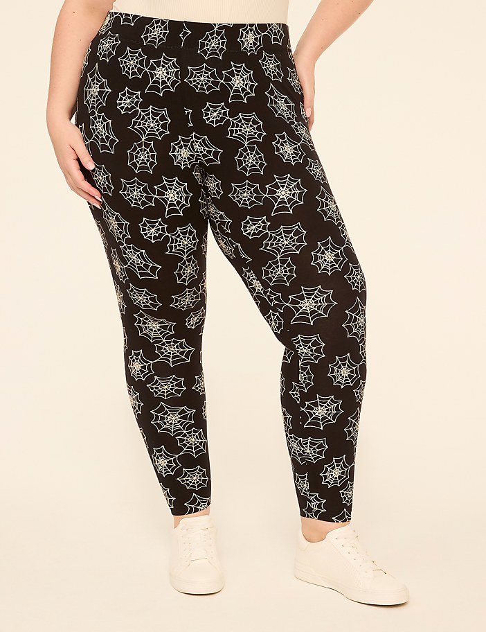 A person wearing black leggings with a white spiderweb pattern stands against a plain, light-colored background.