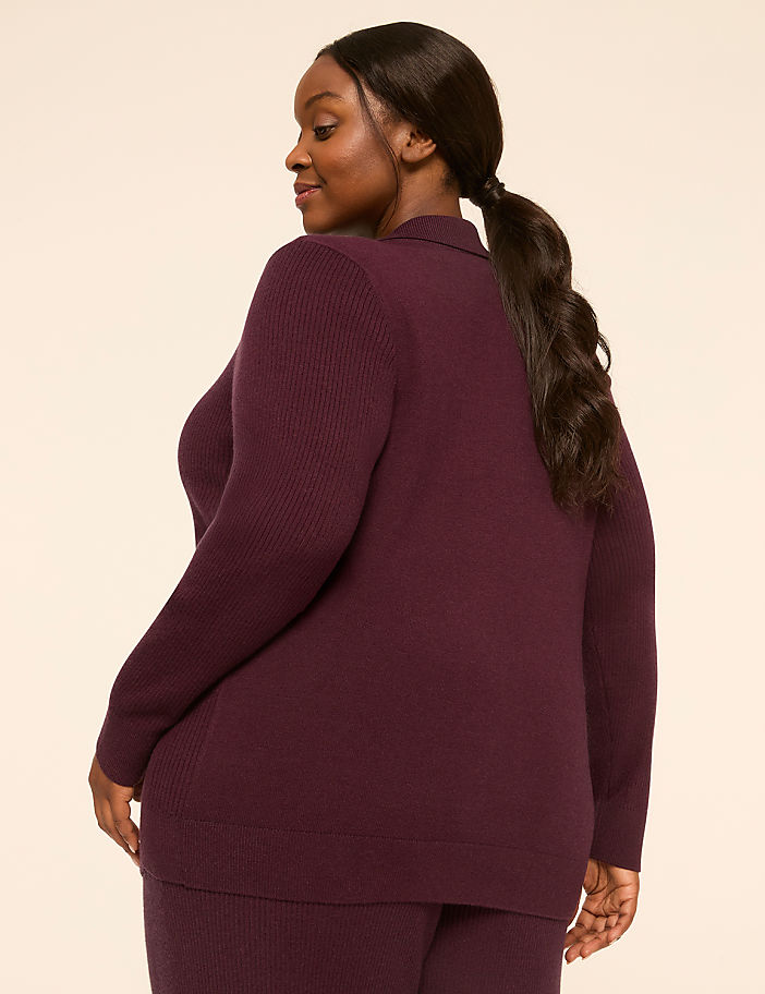 A woman in a plum-colored ribbed cardigan and pants stands against a plain, light-colored background.