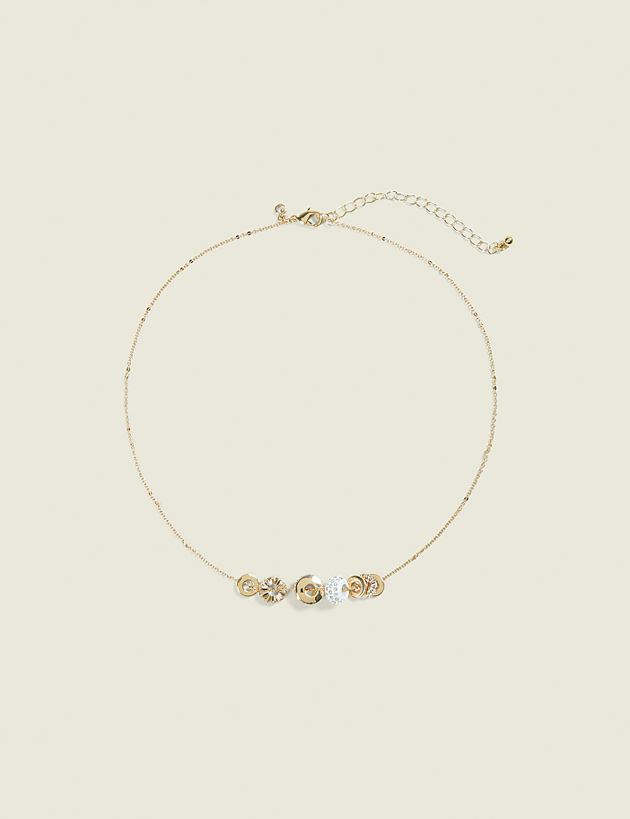 A delicate gold necklace with five circular, jeweled charms rests on a pale yellow background.