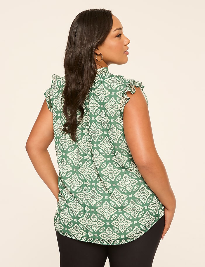 A woman in a green patterned blouse stands against a plain, light-colored background.