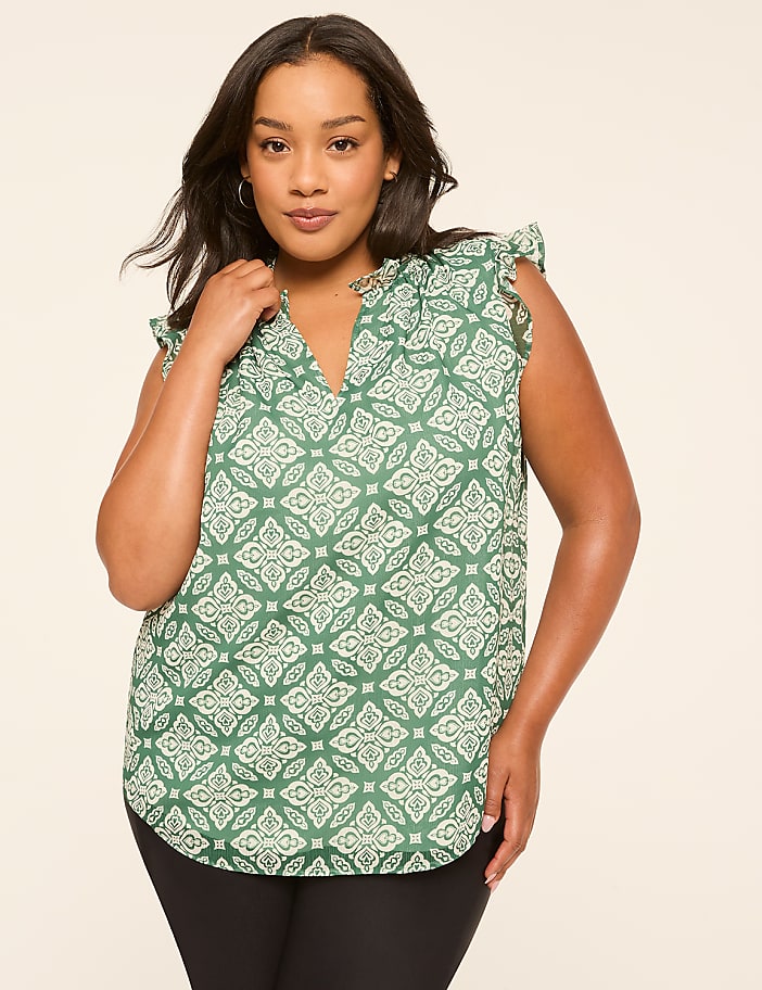 A woman in a green patterned blouse stands against a plain, light-colored background.