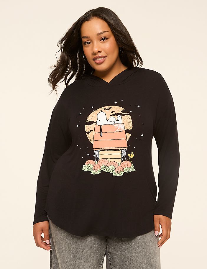 A woman in a black hoodie with a Snoopy Halloween graphic stands against a plain background.