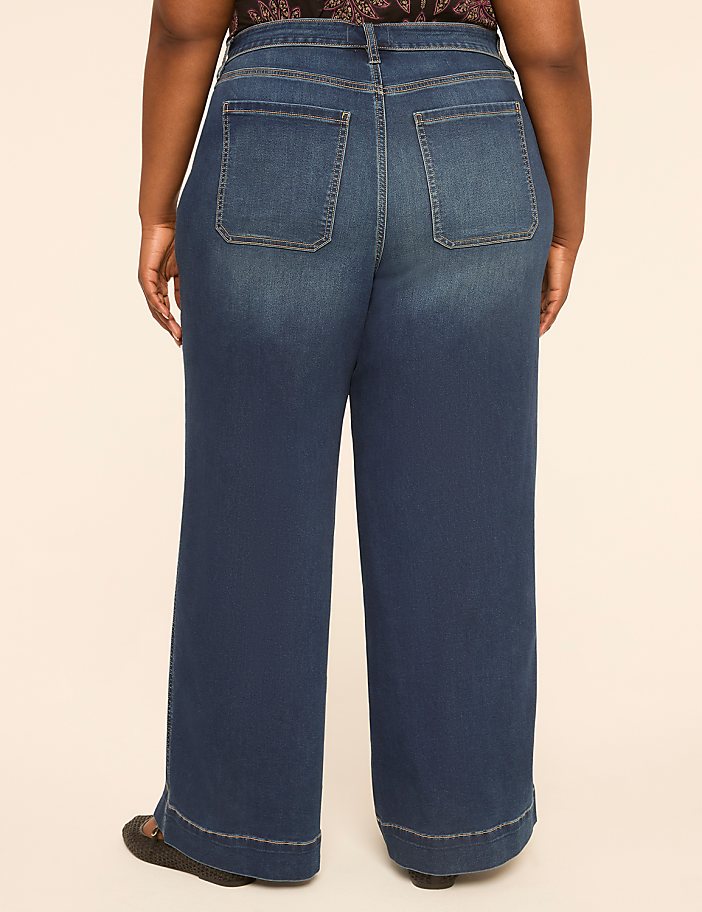 A person wearing wide-leg blue jeans stands against a plain, light-colored background.