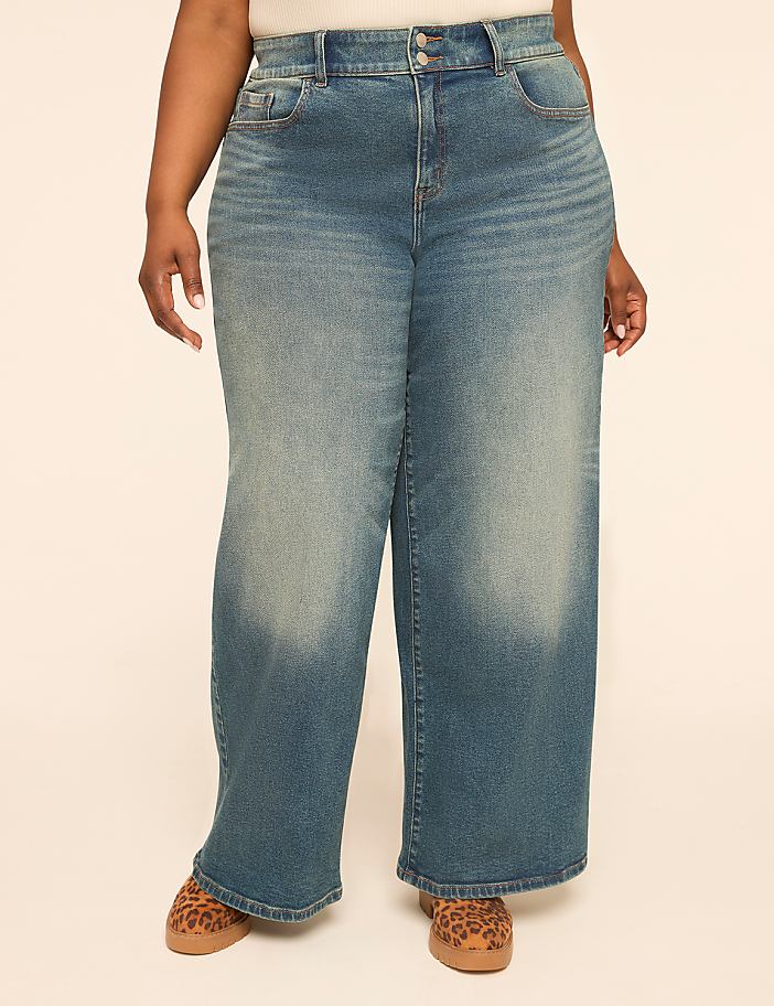 A person stands in wide-leg blue jeans and leopard print shoes against a plain, light-colored background.