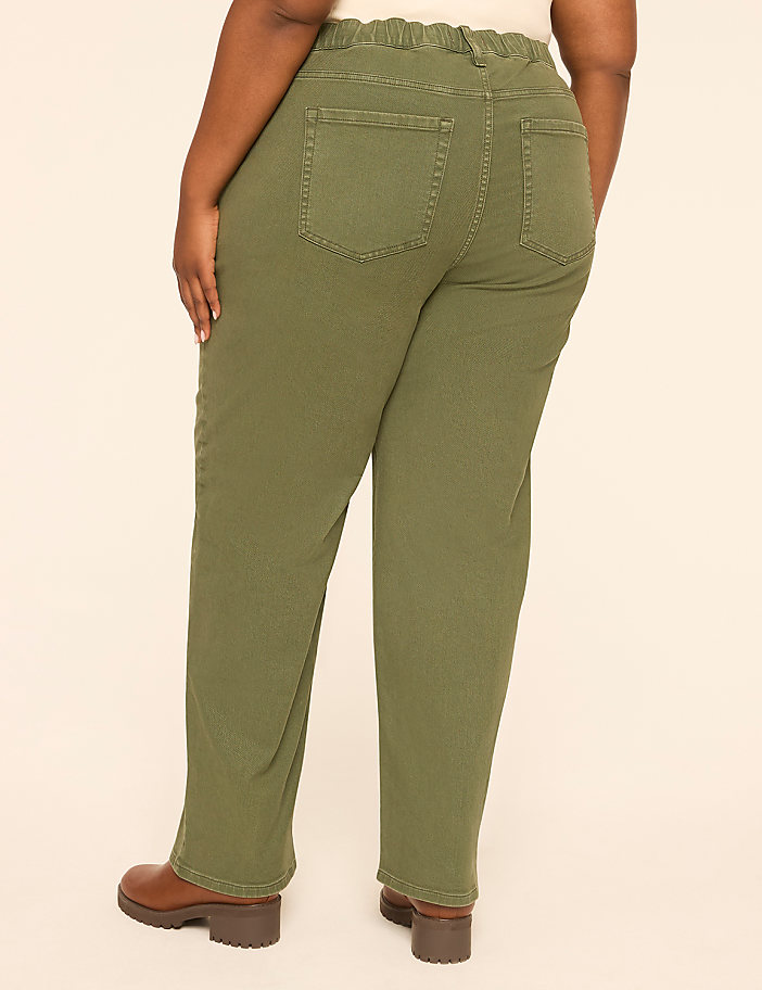 A person wearing olive green pants and brown boots stands against a plain beige background.
