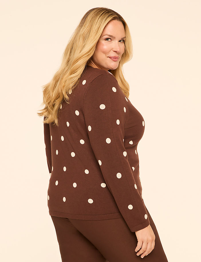 A woman in a brown polka dot sweater and matching pants poses against a plain, light brown background.