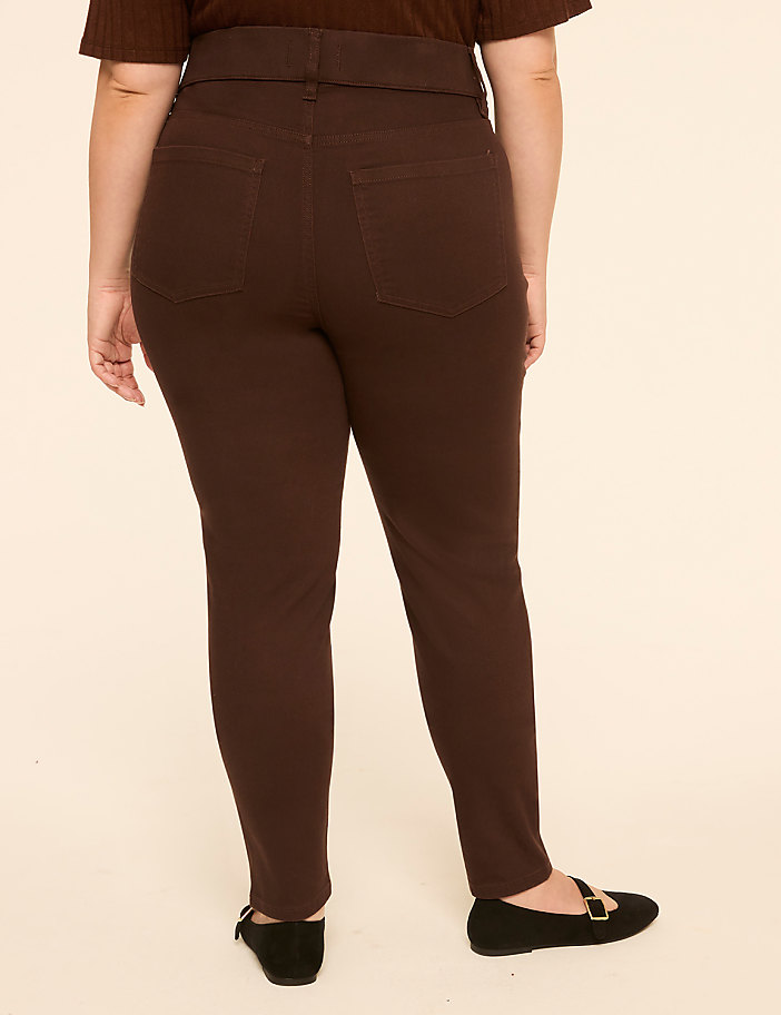 A person wearing brown pants and black flats stands against a plain, light-colored background.