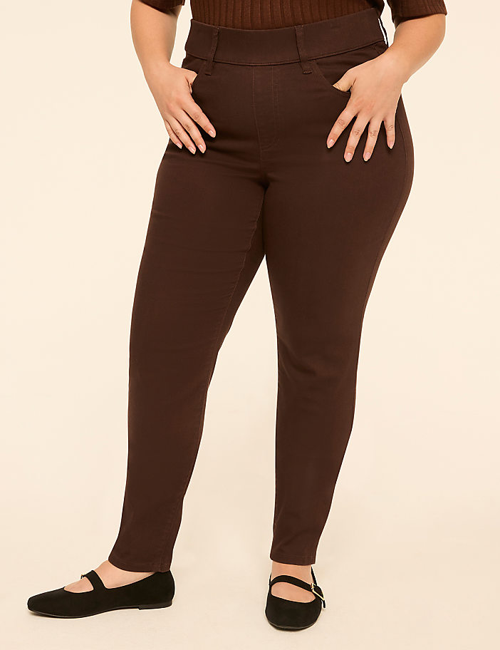 A person wearing brown pants and black flats stands against a plain, light-colored background.