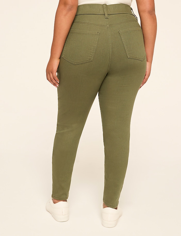 A person wearing olive green skinny jeans and white sneakers stands against a plain, light-colored background.