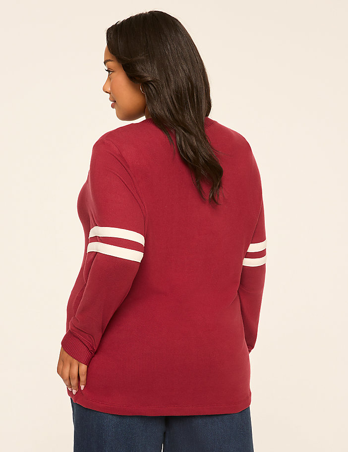 A woman in a maroon long-sleeved shirt with white stripes on the sleeves stands against a plain, light-colored background.