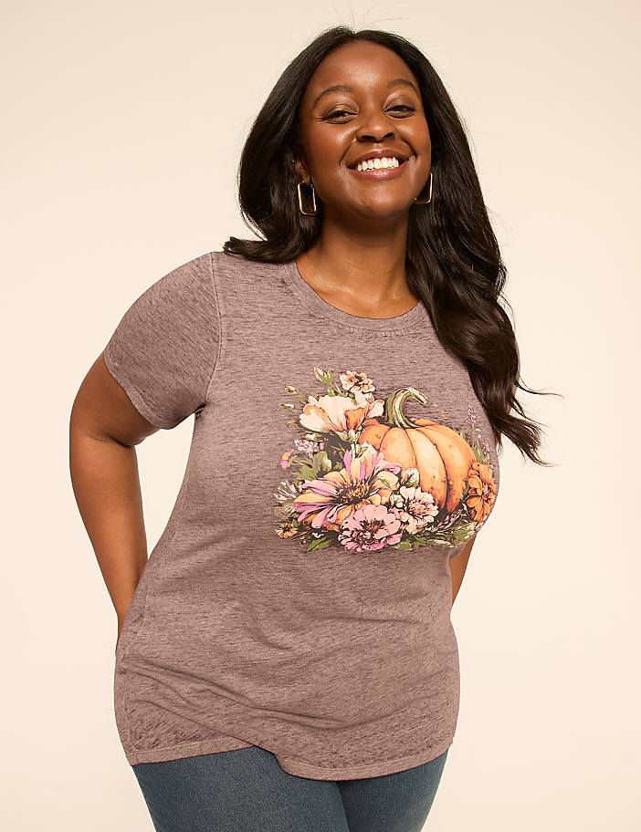 A smiling woman in a t-shirt with a pumpkin and floral design stands against a plain, light-colored background.