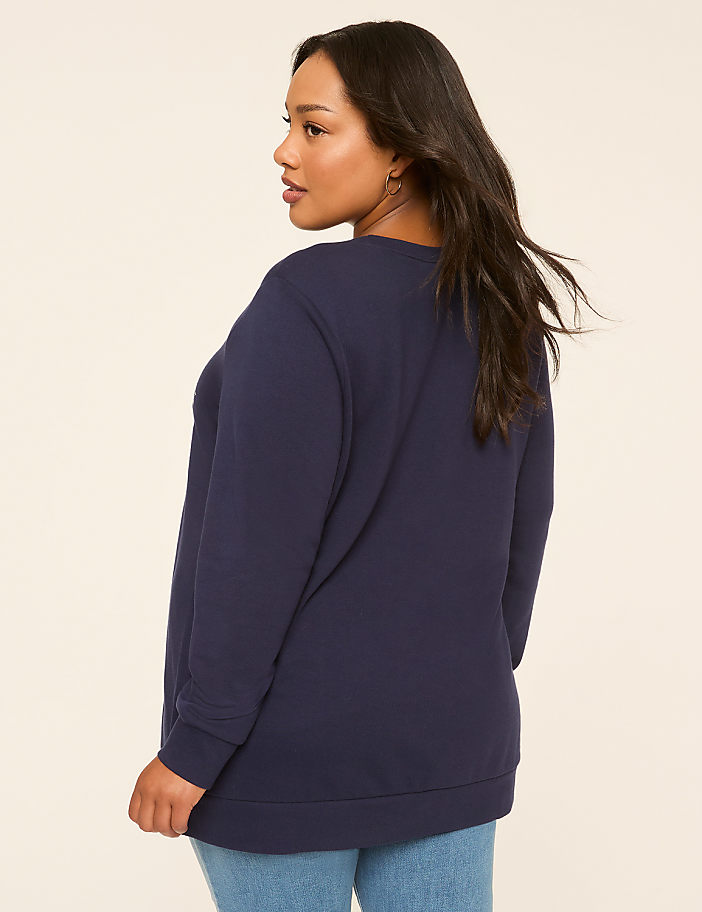 A woman in a navy sweatshirt and jeans stands against a plain, light-colored background.