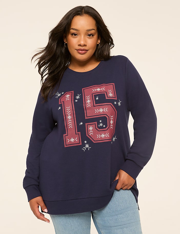 A woman in a navy sweatshirt with a large "15" graphic stands against a plain, light-colored background.