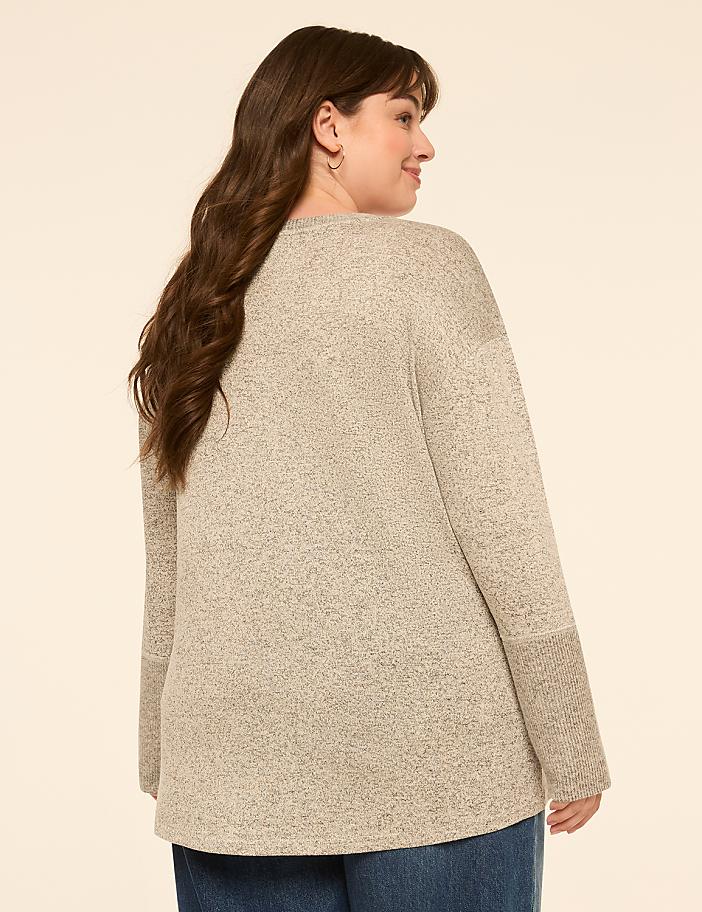 A woman in a heather gray sweater and blue jeans is shown from the back against a plain, light beige background.