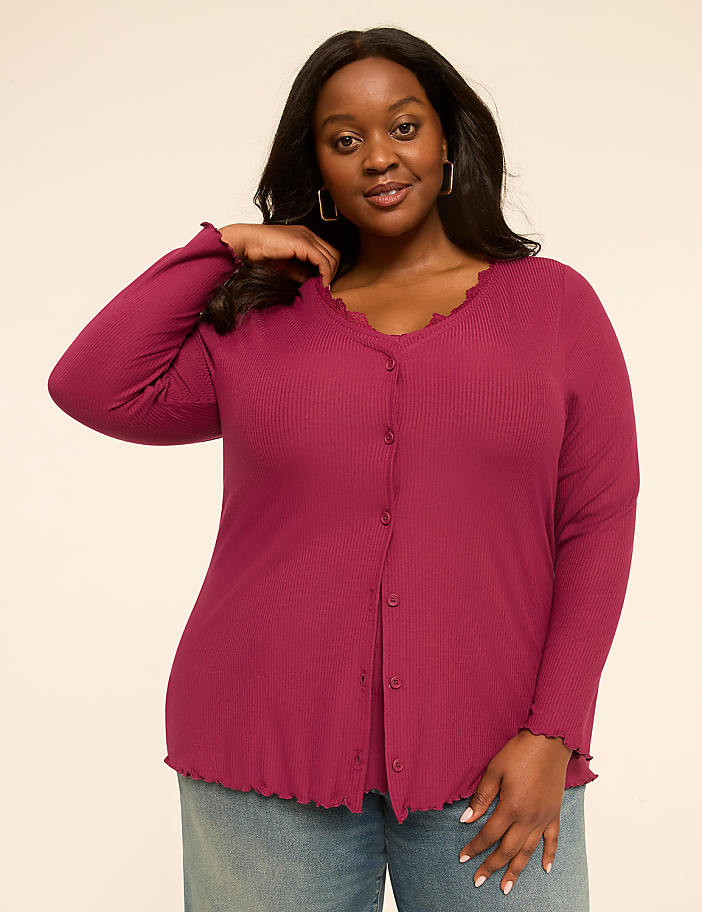 A woman in a magenta ribbed cardigan and blue jeans poses against a plain, light-colored background.