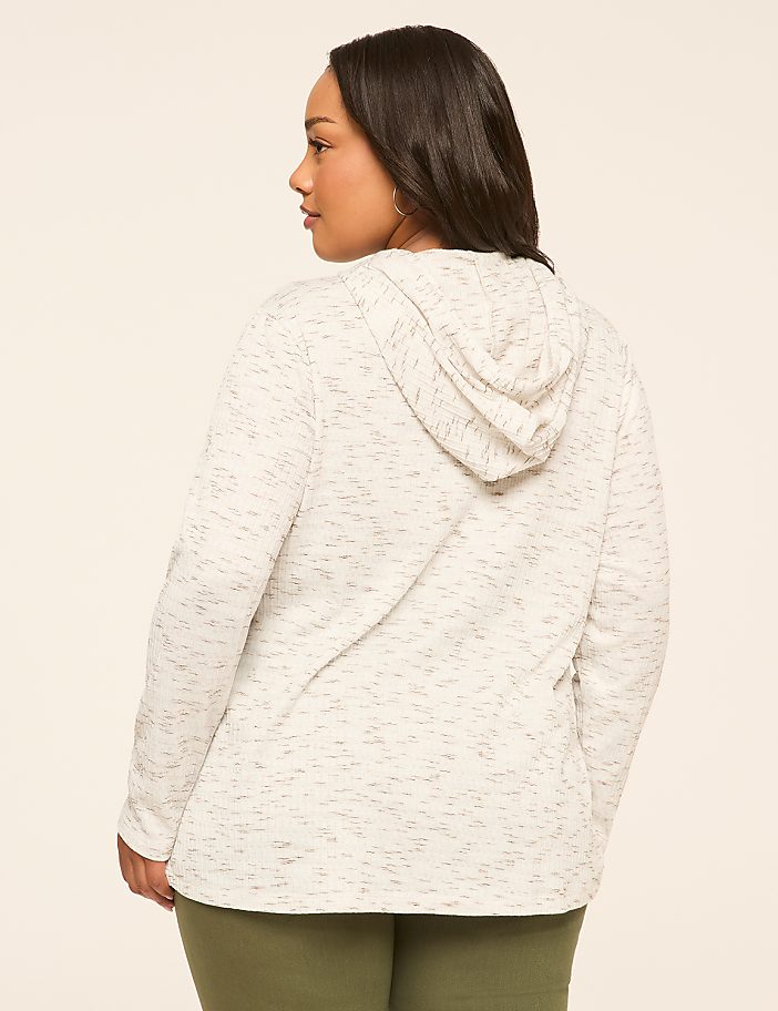 A woman in a speckled white hoodie and olive green leggings stands against a plain, light-colored background.