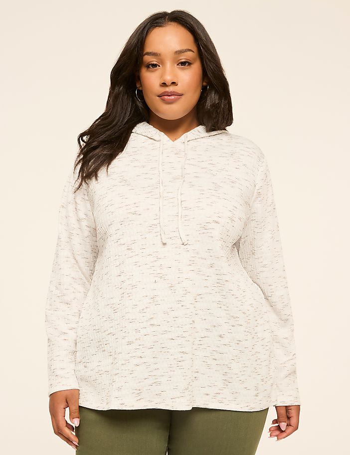 A woman in a speckled grey hoodie stands against a plain, light-colored background.