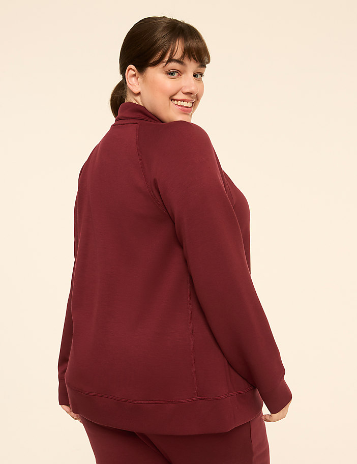 A smiling woman in a maroon sweatshirt stands against a plain, light-colored background.