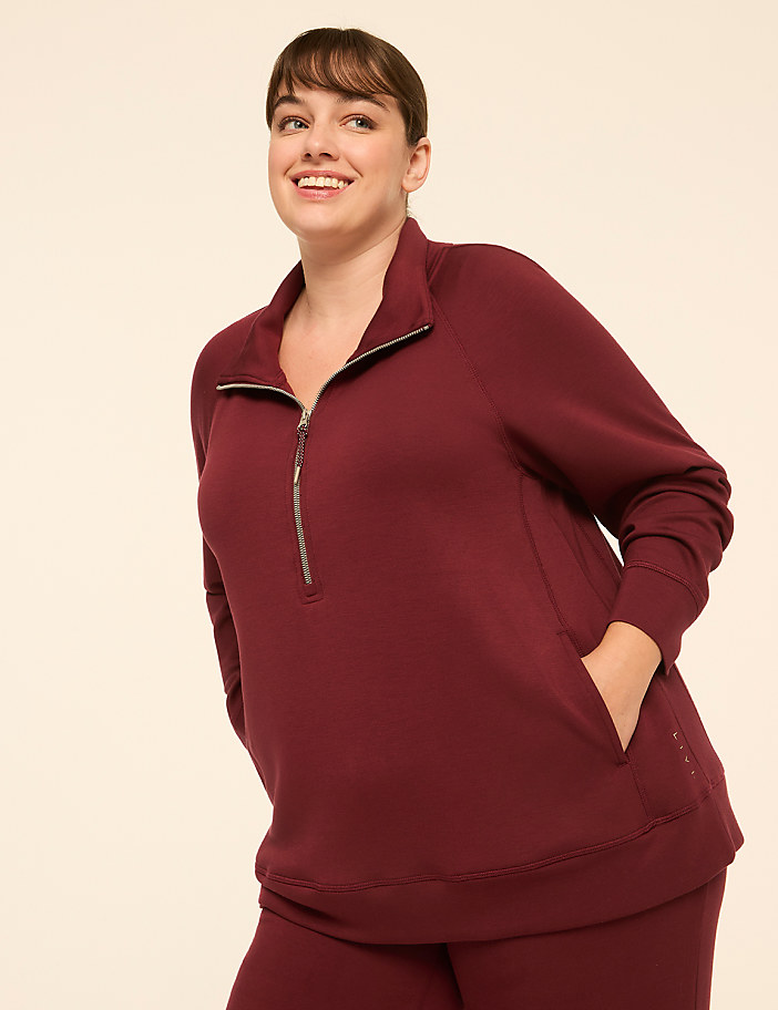 A smiling woman in a maroon quarter-zip sweatshirt stands against a plain, light-colored background.