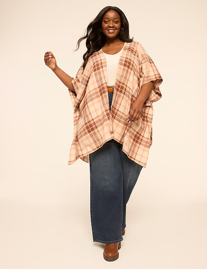 A woman in a plaid kimono and wide-leg jeans smiles against a plain, light background.