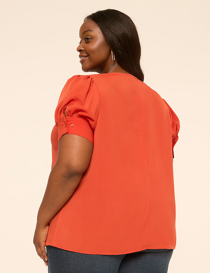 A woman in an orange top stands against a plain, light-colored background.