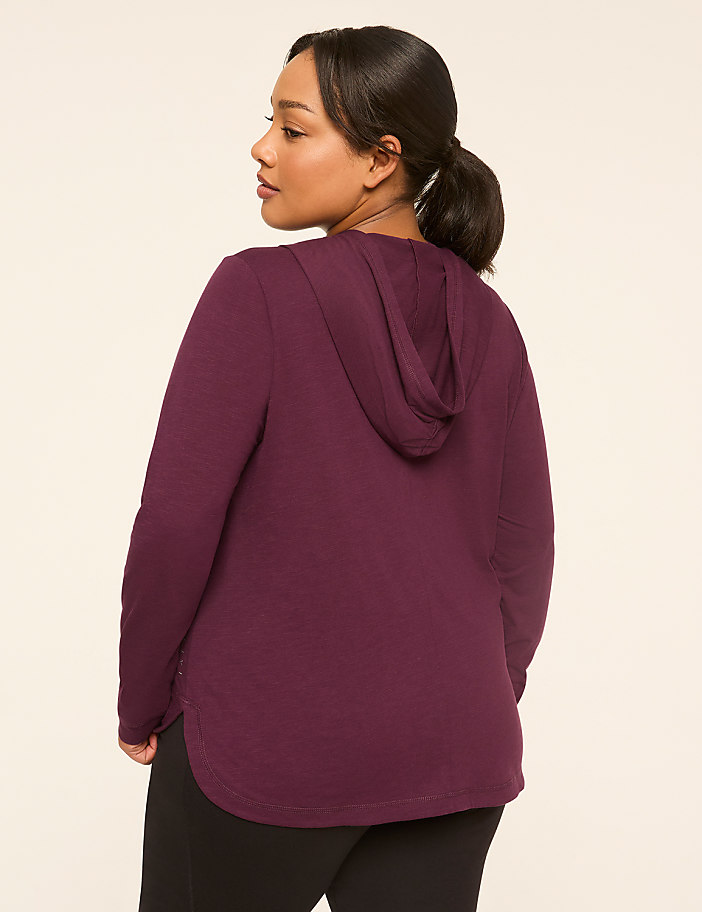 A woman in a purple hoodie stands against a plain, light-colored background.