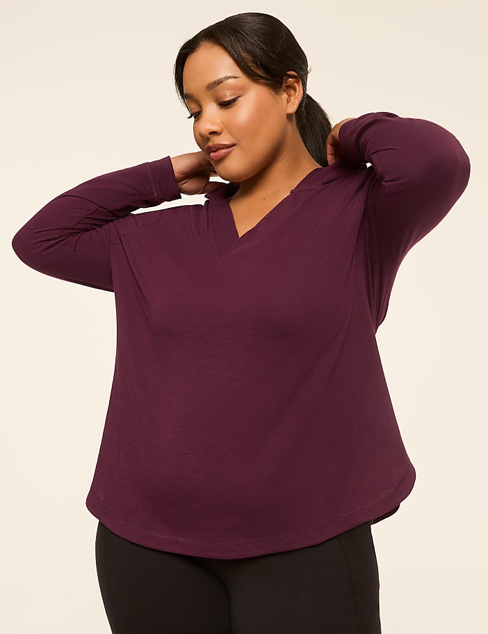 A woman in a purple hoodie adjusts her collar against a plain beige background.