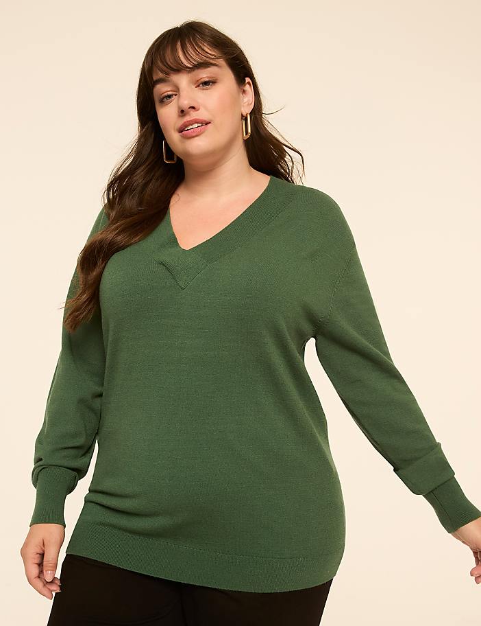 A woman in a green v-neck sweater stands against a plain, light-colored background.