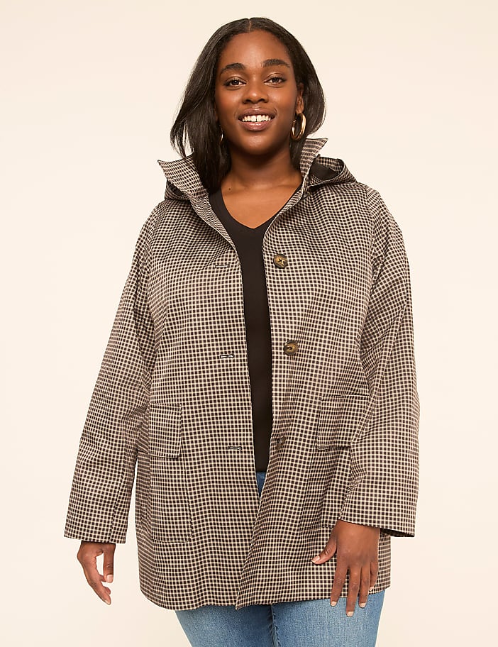 A smiling woman in a patterned jacket stands against a plain, light-colored background.