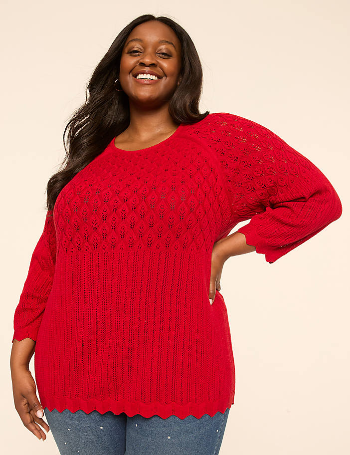 A smiling woman in a red sweater stands against a plain, light-colored background.
