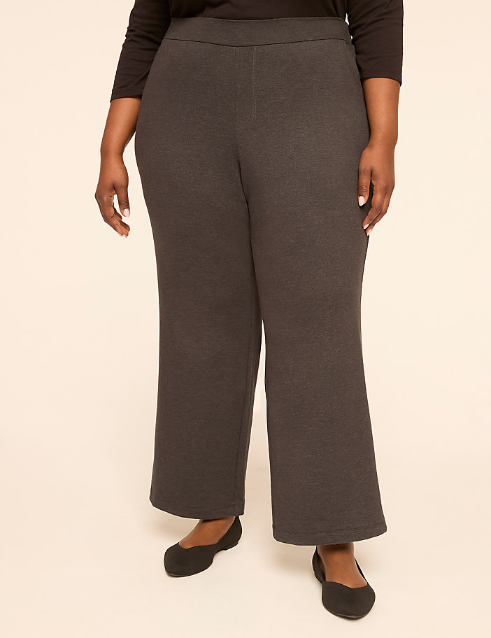 A person stands in dark gray wide-leg pants and black ballet flats against a plain, light-colored background.