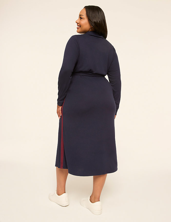 A woman in a navy blue dress with white sneakers stands against a plain, light-colored background.
