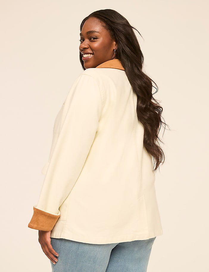 A smiling woman in a cream jacket with brown accents poses against a plain, light-colored background.